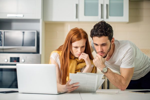 Family managing budget, reviewing their bank accounts using laptop in kitchen