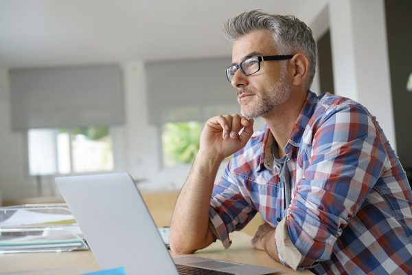 Man wearing glasses sits at a desk, focused on his laptop while working from home